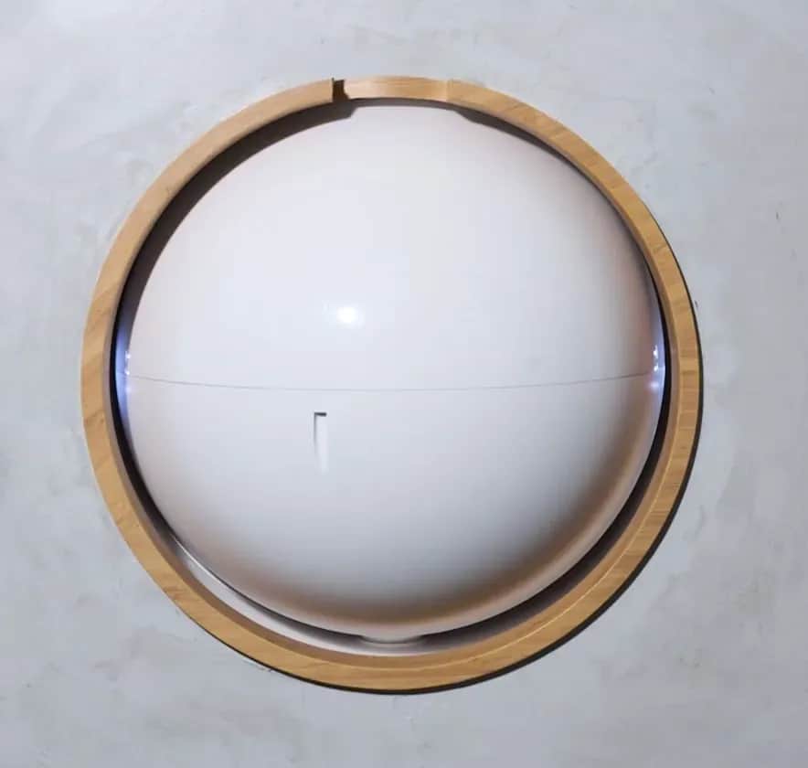 Bamboo Bowls pod closed, a smooth white sphere framed by a light-wood ring in a concrete wall.